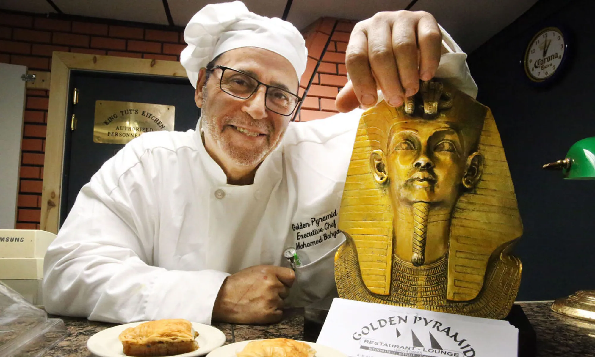 Chef Moe in his Golden Pyramid chef coat, smiling beside an Egyptian pharaoh ornament.