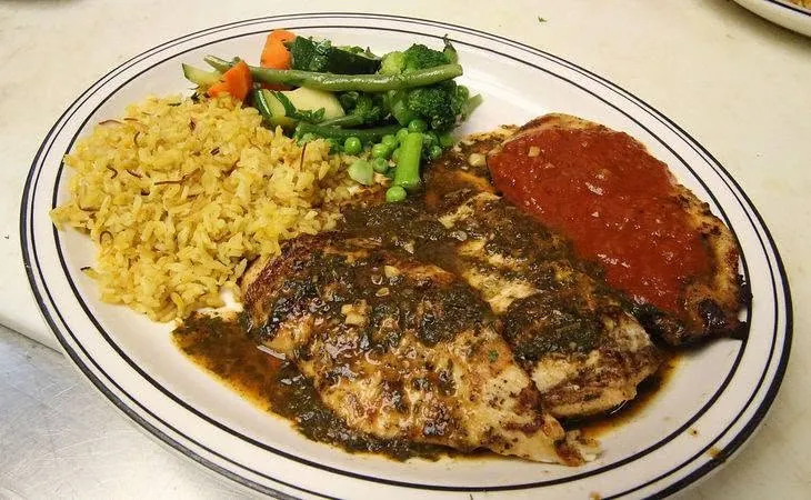 Egyptian chicken with sauce, yellow rice and mixed vegetables on a white plate.