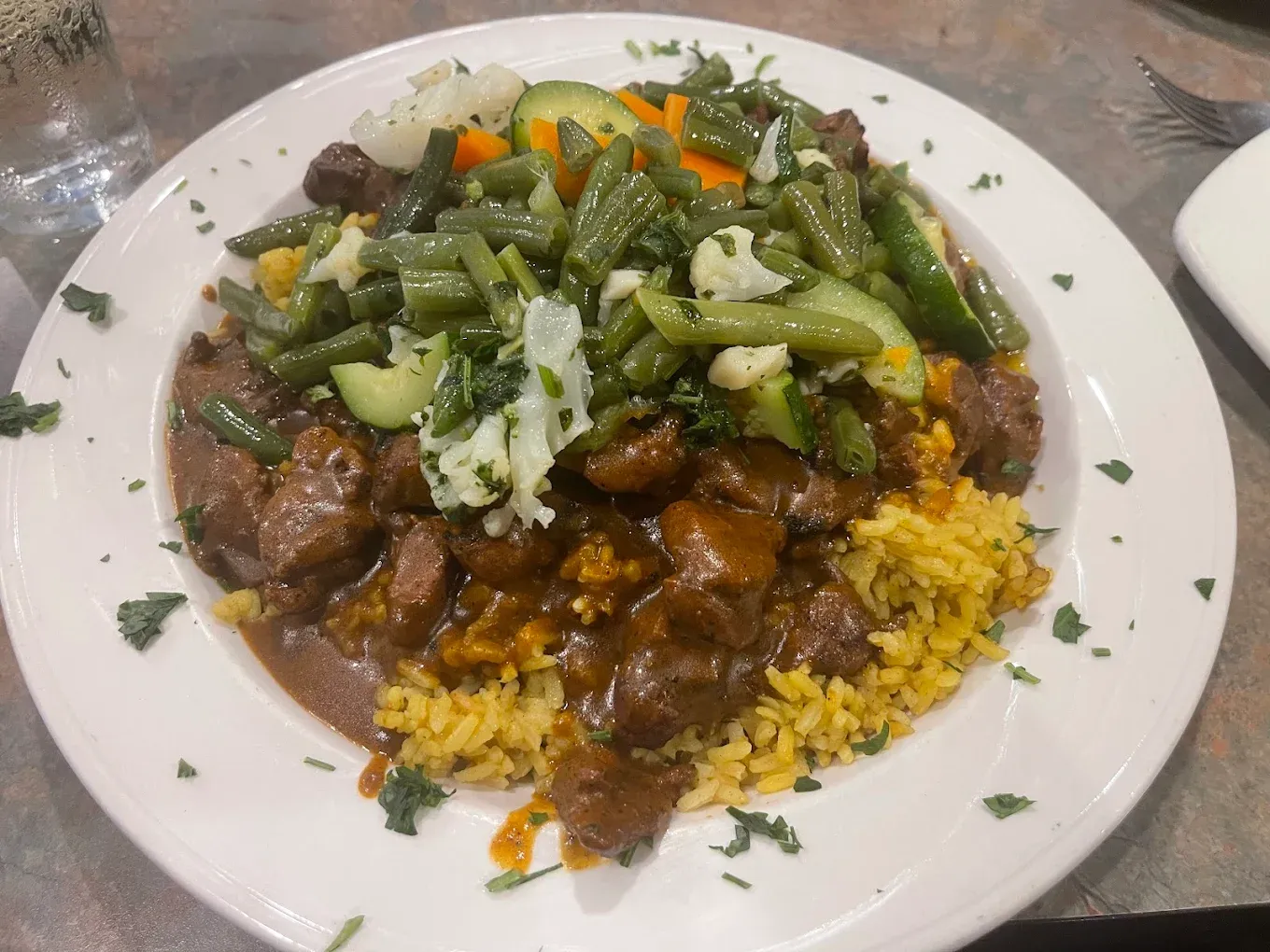 Lamb stew served over yellow rice with green beans and mixed vegetables.